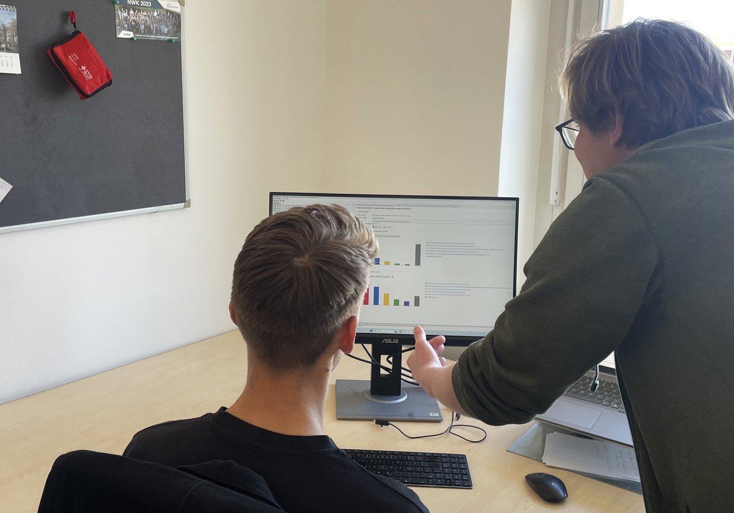 Mitarbeiter und Student werten gemeinsam  die dargestellten Diagramme auf einem Bildschirm aus.